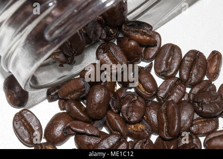 dark roasted coffee beans pouring out of a glass jar on white background Stock Photo