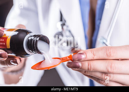 Hands of young woman doctor pouring medicinal syrup on spoon. Stock Photo