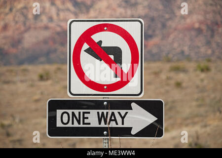 one way and no left turn signs in red black and white with out of focus mountains behind Stock Photo