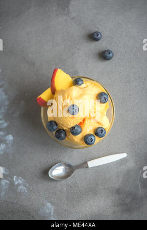 Mango Ice Cream or Sorbet with Blueberries in bowl. Homemade fruit mango ice cream on gray background, copy space.