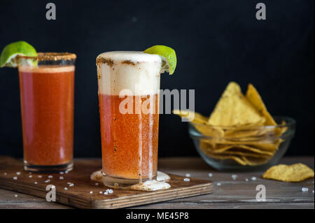 Michelada (Mexican Bloody Beer) with Spisy Rim and Tomato Juice served with Limes and Nacho Chips. Summer Alcohol Cocktail Michelada. Stock Photo