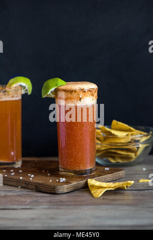 Michelada (Mexican Bloody Beer) with Spisy Rim and Tomato Juice served with Limes and Nacho Chips. Summer Alcohol Cocktail Michelada. Stock Photo