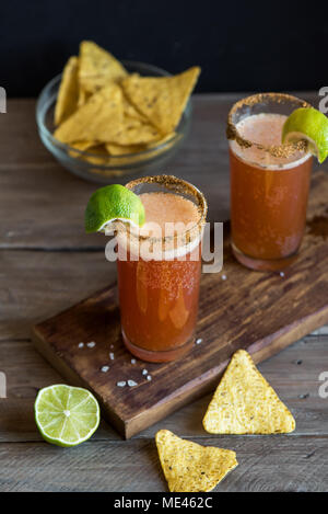 Michelada (Mexican Bloody Beer) with Spisy Rim and Tomato Juice served with Limes and Nacho Chips. Summer Alcohol Cocktail Michelada. Stock Photo