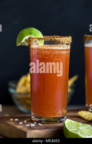 Michelada (Mexican Bloody Beer) with Spisy Rim and Tomato Juice served with Limes and Nacho Chips. Summer Alcohol Cocktail Michelada. Stock Photo