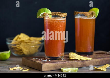 Michelada (Mexican Bloody Beer) with Spisy Rim and Tomato Juice served with Limes and Nacho Chips. Summer Alcohol Cocktail Michelada. Stock Photo