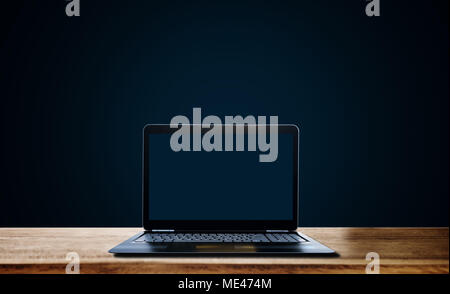 Computer laptop empty blue screen on wooden desk, on dark blue background Stock Photo