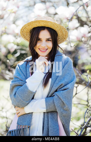 Young girl in hat near blooming magnolia tree on blurred background Stock Photo