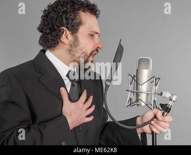 portrait of young man in suit singing with the studio microphone. Isolated on grey background. Singer concept. Stock Photo