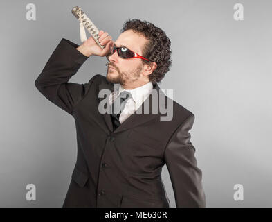 Businessman with sword isolated on grey, aggressive lawyer with Japanese sword, defiant and defensive attitude Stock Photo