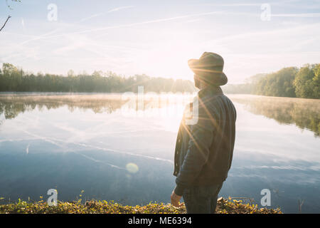Young man contemplating nature by the lake at sunrise, springtime, France, Europe. People travel relaxation in nature concept. Toned image