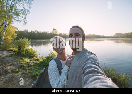 Young couple taking a selfie portrait by the lake. People travel sharing communication concept. Shot in France, Europe. Stock Photo