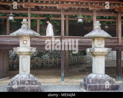 Japanese Shinto priest in traditional costume carrying a heavy bag down ...