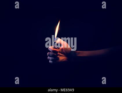 Hand holding lit lighter in the dark Stock Photo