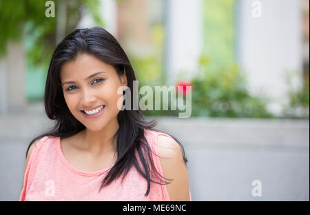 Closeup portrait of confident smiling happy pretty young woman in pink dress, isolated background of blurred trees, flowers. Positive human emotion fa Stock Photo