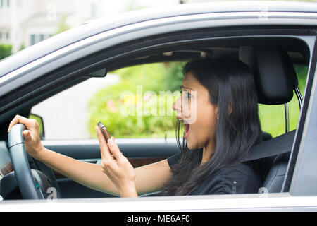 Closeup portrait, young woman driving in black car and checking her phone, then shocked almost about ot have traffic accident, isolated outdoors backg Stock Photo