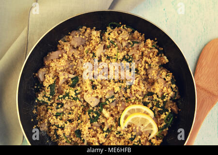 Vegetarian couscous with mushrooms and spinach. Vegan dish with millet in the frying pan. Top view. Stock Photo
