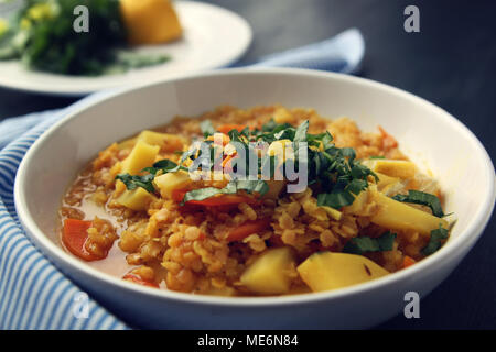 Red lentil stew with potato, carrot and turmeric. Toned photo. Healthy lunch on the round white plate. Colorful vegan dish with potato, carrot and tur Stock Photo