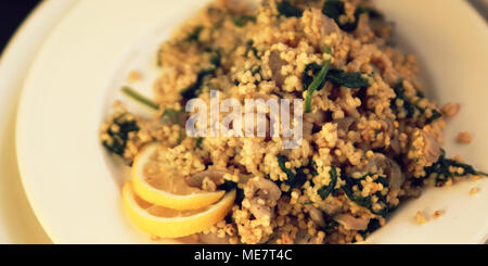 Millet with mushrooms and spinach. Vegan dish. Vegetarian couscous on the round white plate. Wide photo. Stock Photo