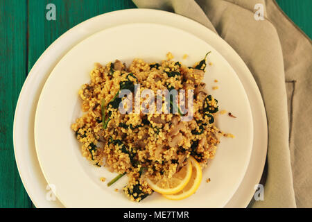Millet with mushrooms and spinach. Jewish cuisine. Vegetarian couscous on the round white plate. Top view. Stock Photo