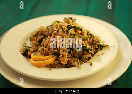 Millet with mushrooms and spinach. Vegan dish. Vegetarian couscous on the round white plate. Stock Photo
