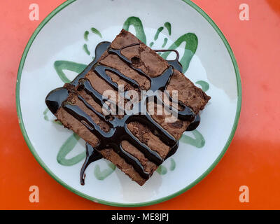 Brownie with Chocolate Sauce Served at Cafe Shop on Orange Surface. High Calorie Food. Stock Photo