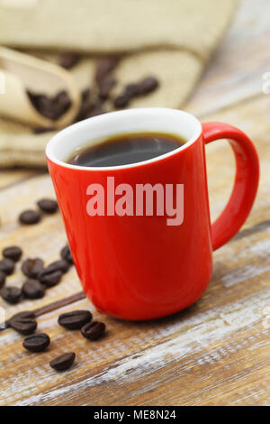 Black coffee in red mug on rustic wooden surface and scattered roasted coffee beans Stock Photo