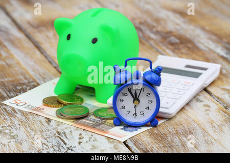 Miniature clock showing five to twelve with money, piggy bank and calculator Stock Photo