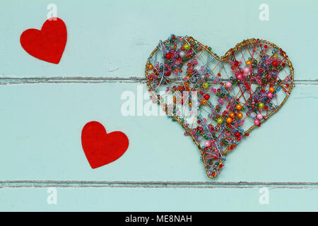 Heart made of colorful beads and two little red hearts on rustic wooden surface Stock Photo