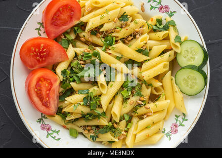 Plate with pasta, seasoned with dill parsley and greens, sliced cucumbers. View from the top, on a black background. Stock Photo