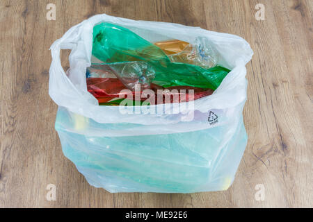 Colorful PET bottles on wood floor. Ecological separation of household garbage. Wrinkled plastic waste in a carrier bag. View from above. Stock Photo