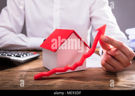 Businessperson's Hand Holding Red Arrow In Front Of House Model Stock Photo