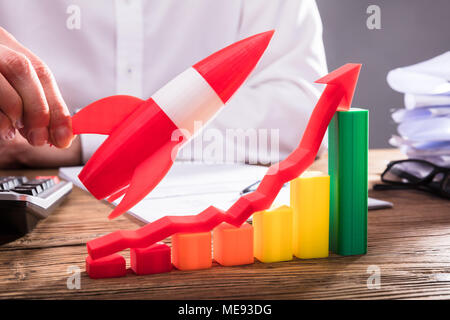 Businessperson's Hand Flying Rocket Over Business Graph With Arrow Symbol Stock Photo