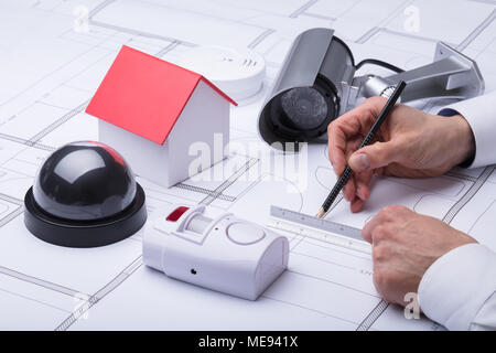 Close-up Of An Architect's Hand Drawing Blueprint Near Security Equipments And House Model Stock Photo