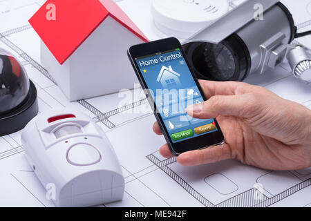 Close-up Of Architect's Hand Using Home Control System On Mobile Phone Over Blueprint Stock Photo