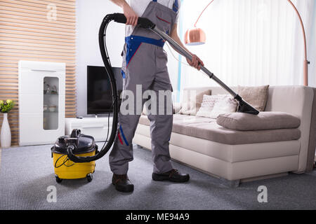 Man Cleaning Sofa In The Living Room Using Vacuum Cleaner At Home Stock Photo