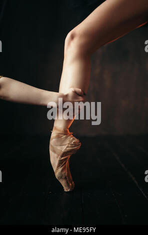 Ballerina hand holds the foot in pointe shoes, black wooden floor. Ballerina in red dress and black practice dancing on the stage in theatre Stock Photo
