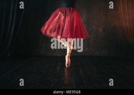 Female ballet dancer legs in pointes. Ballerina in red dress and black practice dancing on the stage in theatre Stock Photo