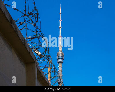 A gray concrete fence with a powerful barbed wire against the backdrop of the Ostankino Tower on a clear, sunny day. Symbolizes the restriction of fre Stock Photo