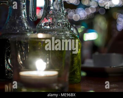 A closely-taken table in a restaurant with a candle and a bottle of vegetable oil green with a blurred background. Romantic setting. Stock Photo