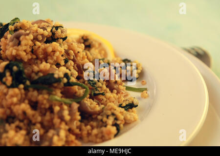 Millet with mushrooms and spinach. Close up. Vegan dish. Vegetarian couscous on the round white plate. Stock Photo