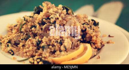 Millet with mushrooms and spinach. Jewish cuisine. Vegetarian couscous on the round white plate. Close up. Wide photo. Stock Photo