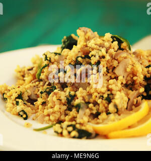 Millet with mushrooms and spinach. Vegan dish. Vegetarian couscous on the round white plate. Close up. Toned photo. Stock Photo