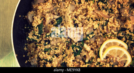 Vegetarian couscous with mushrooms and spinach. Close up. Vegan dish with millet in the frying pan. Top view. Wide photo. Stock Photo