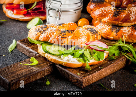 Variety of homemade bagels sandwiches with sesame and poppy seeds, cream cheese,  ham, radish, arugula, cherry tomatoes, cucumbers, with ingredients o Stock Photo