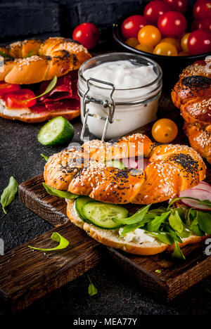 Variety of homemade bagels sandwiches with sesame and poppy seeds, cream cheese,  ham, radish, arugula, cherry tomatoes, cucumbers, with ingredients o Stock Photo