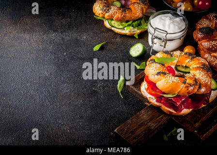 Variety of homemade bagels sandwiches with sesame and poppy seeds, cream cheese,  ham, radish, arugula, cherry tomatoes, cucumbers, with ingredients o Stock Photo