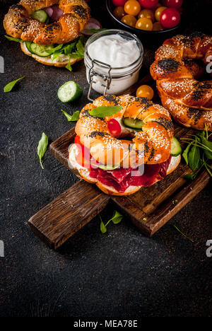 Variety of homemade bagels sandwiches with sesame and poppy seeds, cream cheese,  ham, radish, arugula, cherry tomatoes, cucumbers, with ingredients o Stock Photo