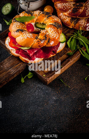 Variety of homemade bagels sandwiches with sesame and poppy seeds, cream cheese,  ham, radish, arugula, cherry tomatoes, cucumbers, with ingredients o Stock Photo