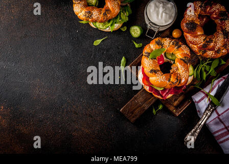 Variety of homemade bagels sandwiches with sesame and poppy seeds, cream cheese,  ham, radish, arugula, cherry tomatoes, cucumbers, with ingredients o Stock Photo