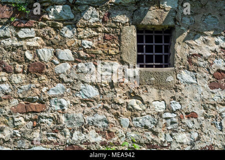 Old dark age stone wall and small prison cell window with bars Stock Photo